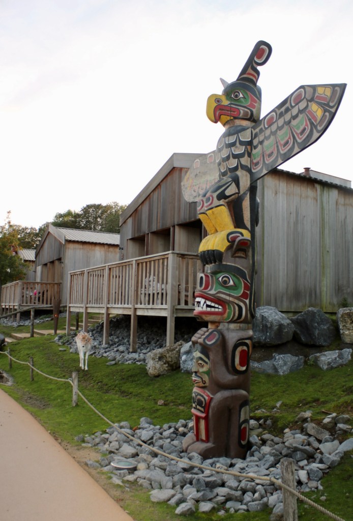 Things Helen Loves, wooden lodge at Pairi Daiza resort built in First Nations style. A colourful carved totem pole with bird at top stands in front of lodge. Pairi Daiza zoo, Belgium