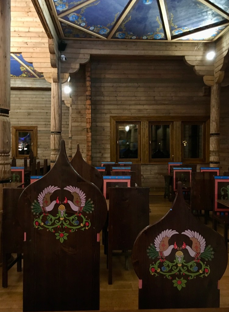 Things Helen Loves, painted wooden seats in Izba restaurant in Pairi Daiza, Belgium. Seats are painted in pinks and blues on brown background in folk Russian inspired style